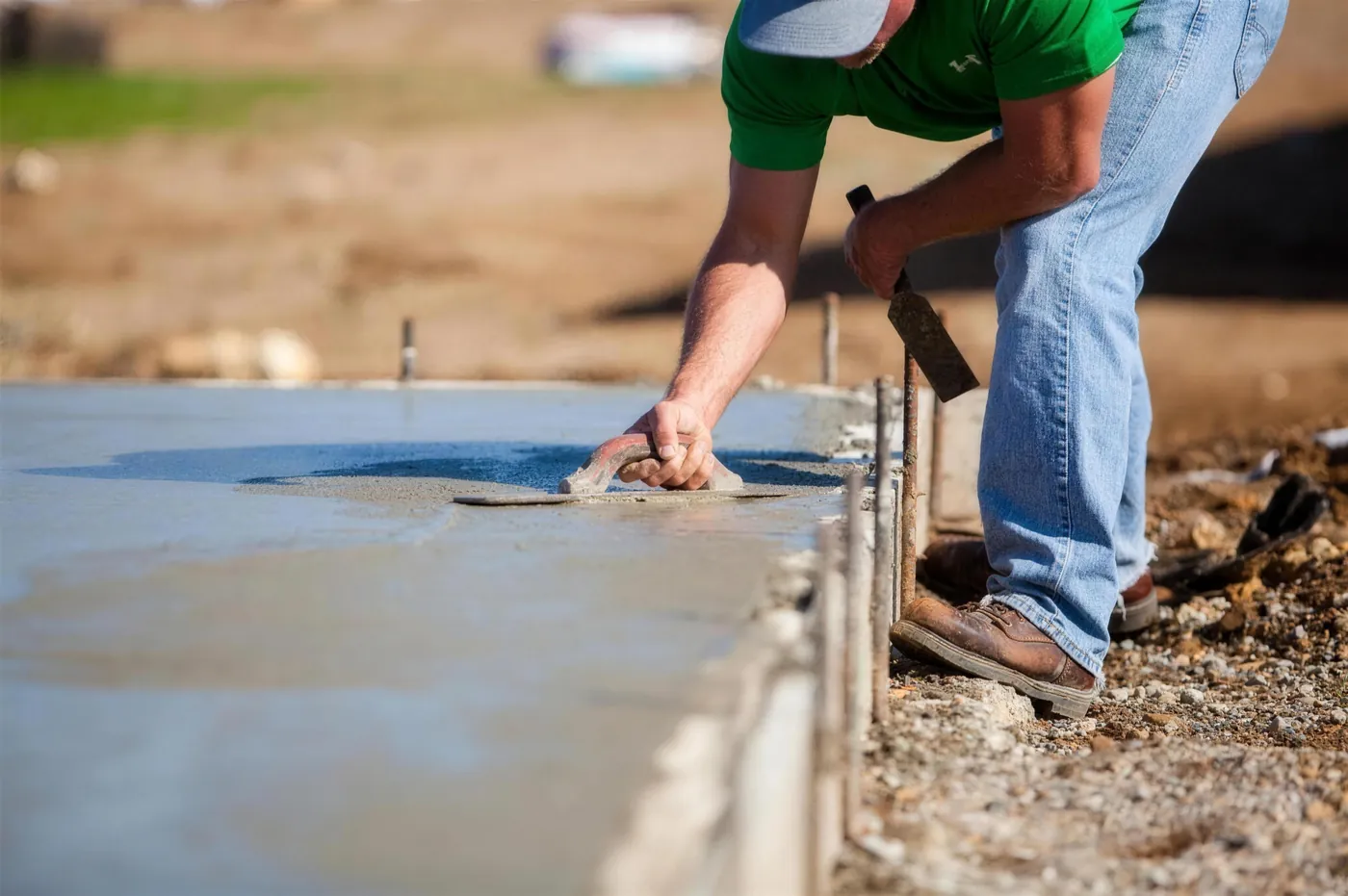 A finisher working the edge of a fresh concrete slab along its forms on an open job site
